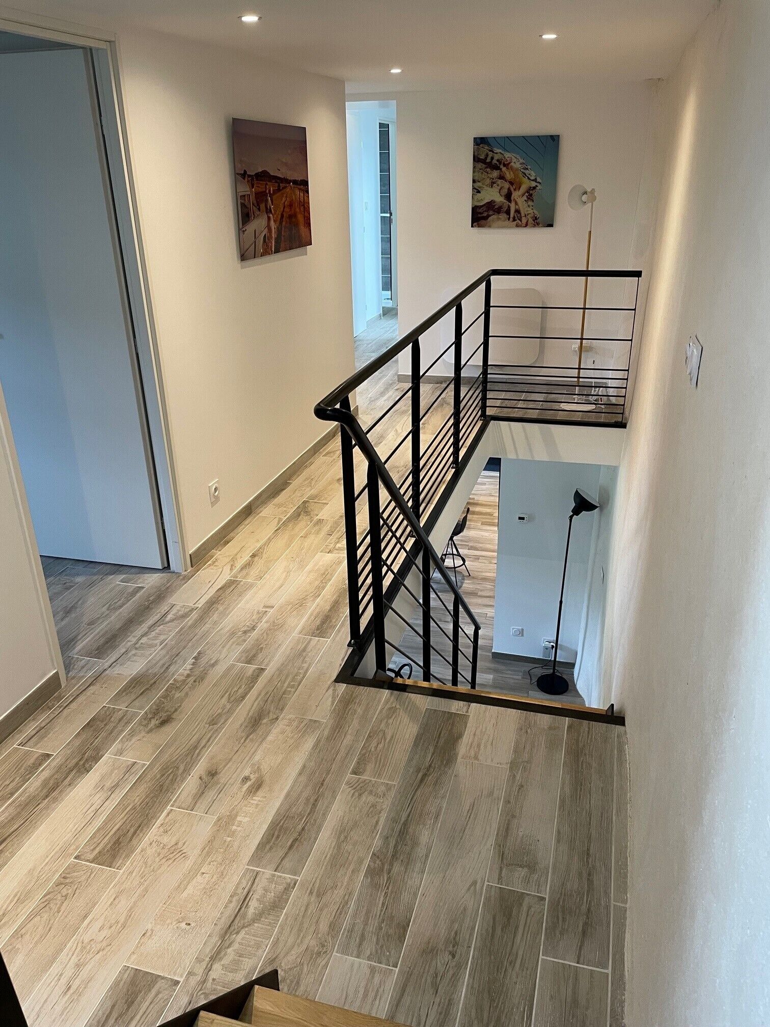 Un interior moderno con piso de madera, una escalera con barandal negro y dos obras de arte enmarcadas en las paredes.