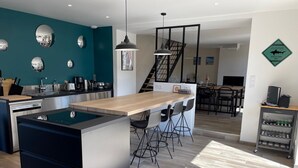 Een moderne keuken met een centraal eiland, een eethoek met barstoelen, en een trap die naar een hoger gelegen verdieping leidt.