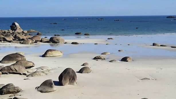 Een strand met grote rotsen en rustig water.