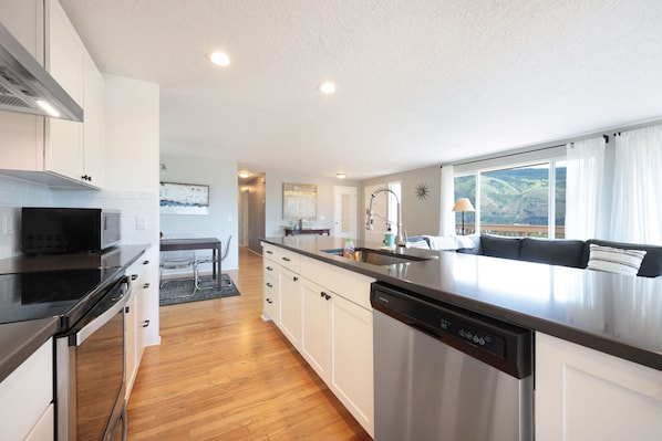 A modern kitchen with stainless steel appliances, white cabinetry, and a large island with a dishwasher.