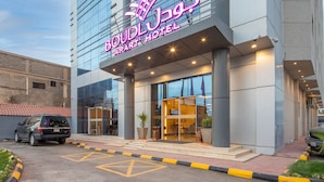 Het exterieur van Hotel Boudou, met een modern design, inclusief een opvallend neonbord, grote ramen en een goed verlichte entree.