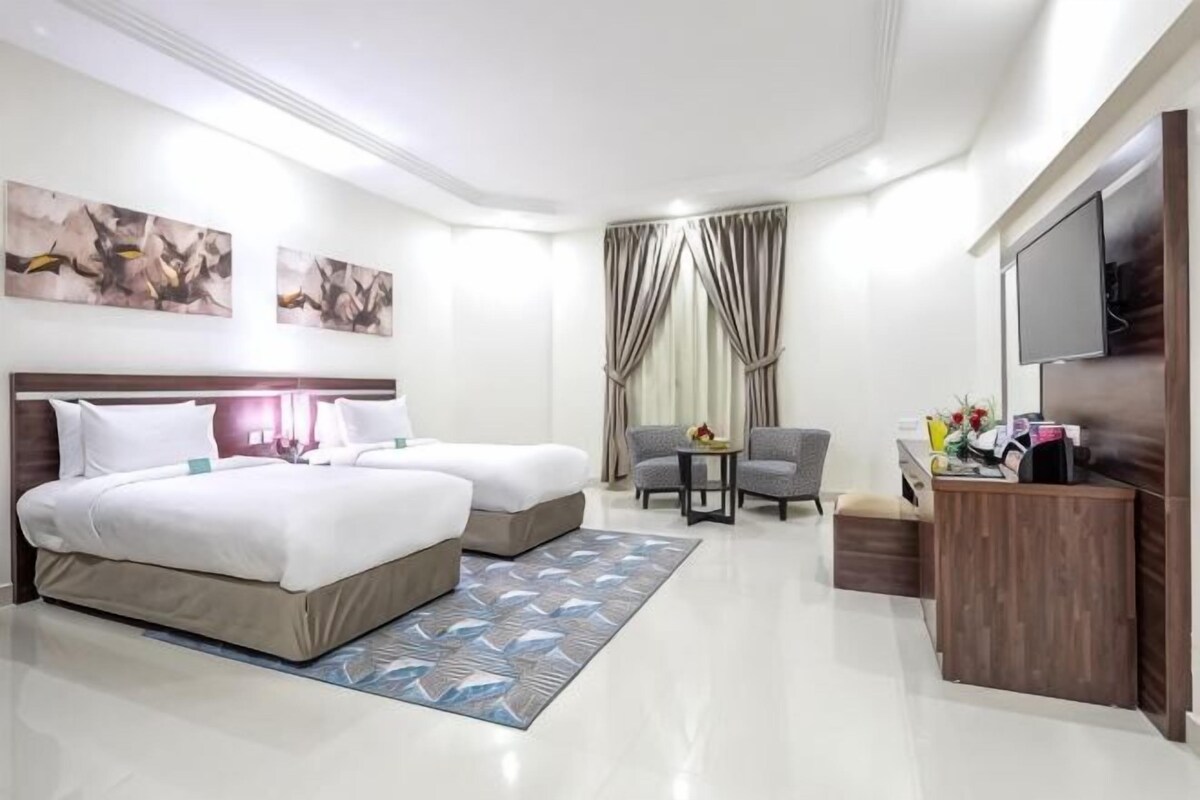 A hotel room with two beds, a TV, a desk, and a chair.