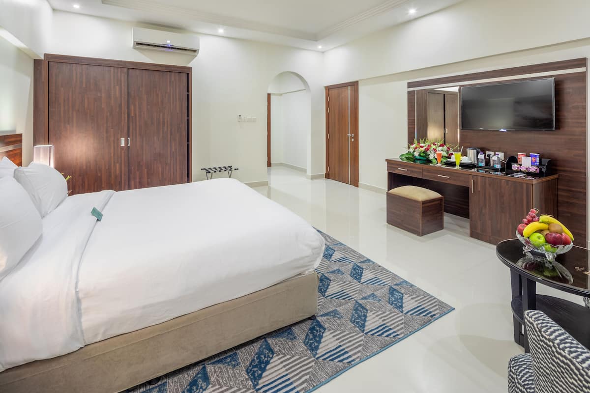 Une chambre d’hôtel dotée d’un grand lit, d’un bureau avec un téléviseur à écran plat, d’une coiffeuse avec des articles de toilette et d’une armoire.