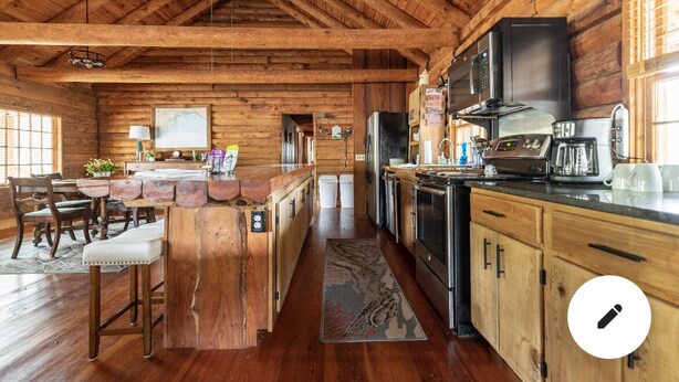 A rustic cabin interior with a wooden bar, dining area, and kitchen. -  Cabin By the Bay A unique authentic log cabin by the beach with fenced yard (Panacea)