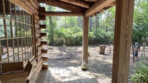 A wooden deck with a covered area, surrounded by greenery. -  Cabin By the Bay A unique authentic log cabin by the beach with fenced yard (Panacea)