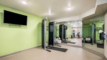 Een sportschool met trainingsapparatuur, een televisie en een spiegel.
