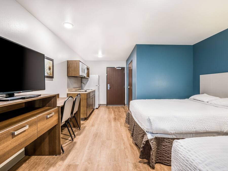 A compact hotel room with a bed, a desk with a computer, a microwave, and a wardrobe.