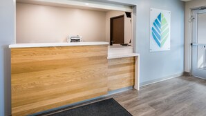 A reception area with a wooden reception desk, a printer, and a wall-mounted logo. - Woodspring Suites Littleton-South Denver (Littleton)