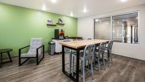 A conference room with a wooden table, six chairs, a small side table, a trash can, and a coffee machine. - Woodspring Suites Littleton-South Denver (Littleton)