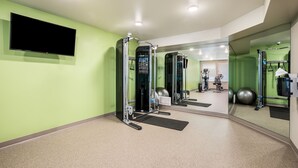 A gym with exercise equipment, a TV, and a mirror. - Woodspring Suites Littleton-South Denver (Littleton)