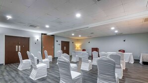 A conference room with rows of chairs covered in white sashes, wooden floors, and a ceiling with recessed lighting. - Suburban Studios Rock Hill Northeast I-77 (Rock Hill)