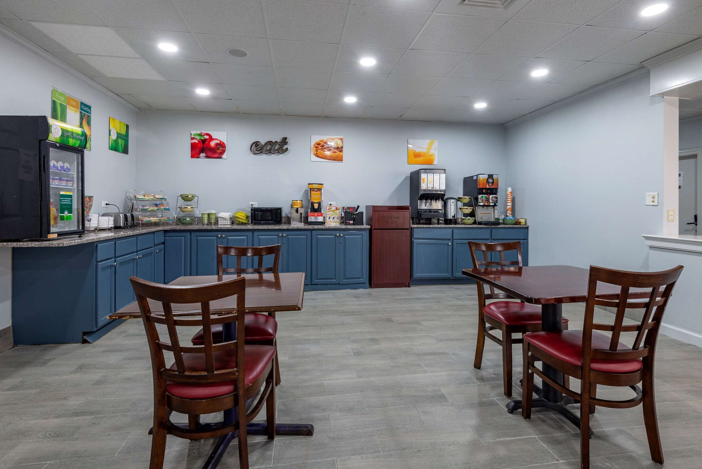 A modern kitchen with blue cabinets, a refrigerator, a coffee machine, and a dining area with wooden chairs and a table.