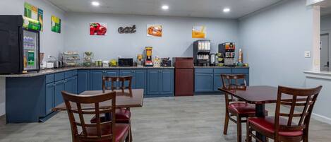A modern kitchen with blue cabinets, a refrigerator, a coffee machine, and a dining area with wooden chairs and a table.