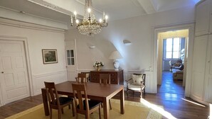 Et spiseområde med et træbord, stole, en lysekrone og udsigt til et andet rum.