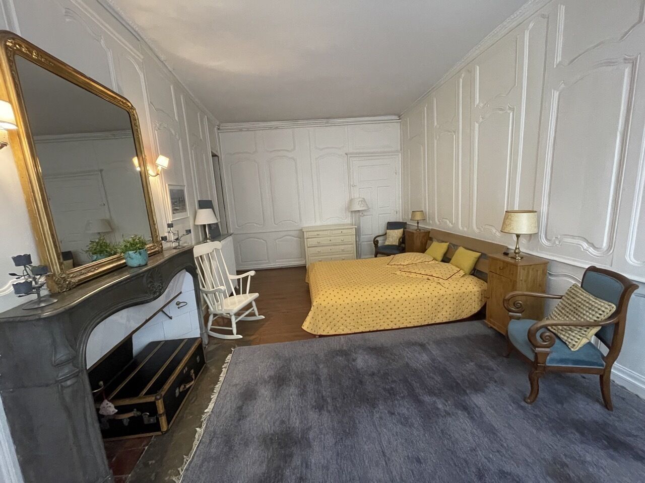 Un dormitorio con chimenea, una cama con colcha amarilla, un aparador y una silla.