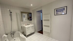 Et moderne badeværelse med badekar, vask og brusebad. Et spejl er anbragt over vasken, og der er en bøjle til håndklæder på væggen.