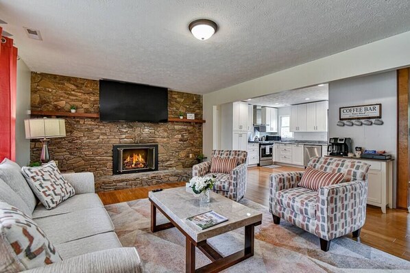 A living room with a fireplace, a coffee bar, and a kitchen in the background.
