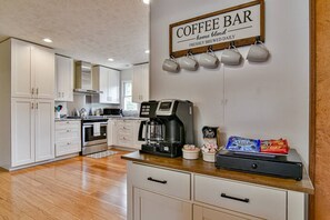 Uma cozinha com armários brancos, um letreiro de café, uma máquina de café e alguns petiscos no balcão.