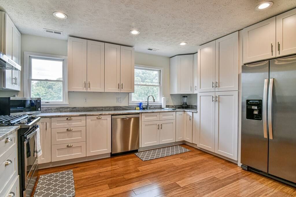 A modern kitchen with white cabinets, stainless steel appliances, and a wooden floor.