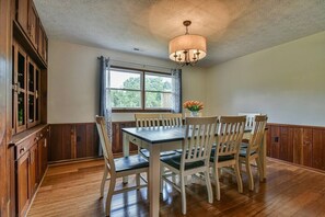 A dining area with a wooden table and chairs, a chandelier, and a window with curtains.