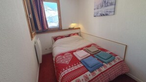 Ein kleines Schlafzimmer mit Bett, einem Fenster mit Vorhängen, einer Wandlampe und einem Bild.