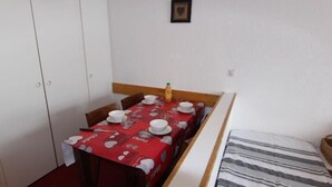 Ein kleines Zimmer mit Esstisch für zwei Personen, einem Bett mit gestreifter Bettwäsche und einem weißen Kleiderschrank.