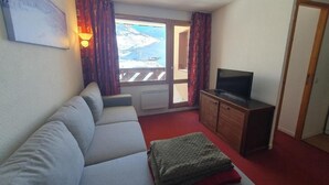 Ein Zimmer mit einer Couch, einem Fernseher, einem Schrank und Blick auf eine verschneite Landschaft durch ein Fenster.