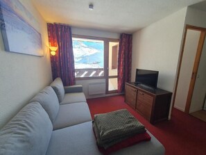 A room with a sofa, a television, a cabinet, and a view of a snowy landscape through a window. - Ski-in/ski-out & foot of the slopes, 1st floor, view mountain, sauna, hammam, balcony, tv, 29m² (Val Thorens)