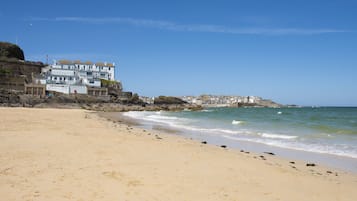 A beach with a large building on the left, featuring multiple balconies and a stone base.