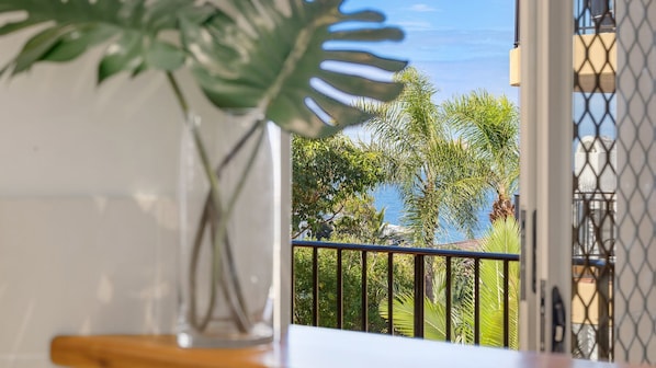 A balcony with a view of palm trees and a building across the water.