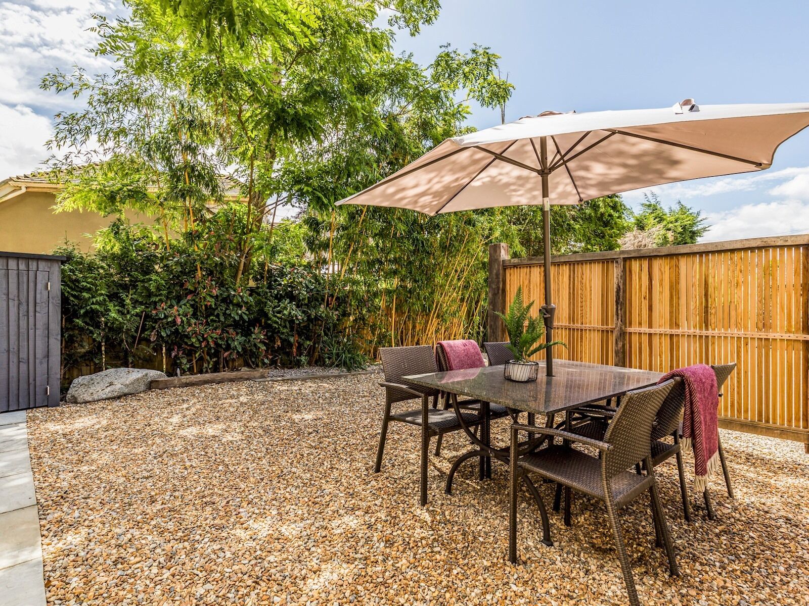 A patio with a table and chairs, a large umbrella, and a wooden fence.