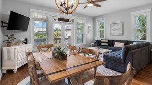 A spacious living area with a wooden dining table, a dark-colored sofa, and a ceiling fan.