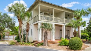 A two-story house with a balcony, surrounded by palm trees and a well-maintained lawn.