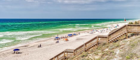 Una playa con un paseo marítimo de madera, arena y vista al océano.