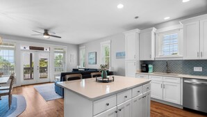 A modern kitchen with white cabinetry, a central island, and a dining area with a blue rug.