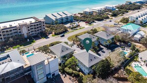 An aerial view of a coastal hotel area with multiple buildings, a road, and a clear view of the ocean.