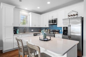 A modern kitchen with white cabinets, a stainless steel refrigerator, and a central island with two chairs.