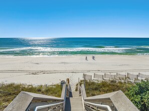 A wooden boardwalk leading to a beach with a clear view of the ocean and two people walking on the sand.
