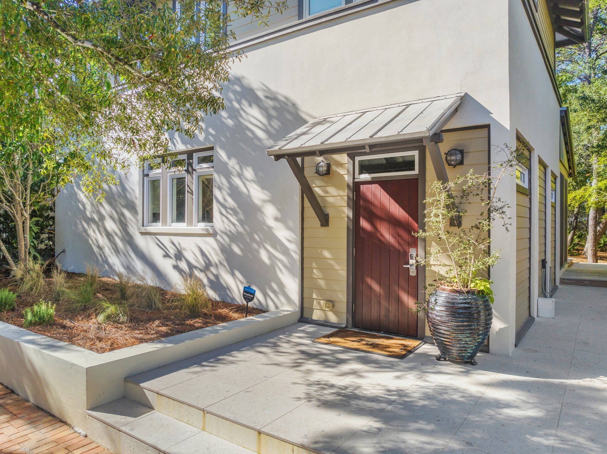 A modern house with a red door, a small porch, and a large potted plant.