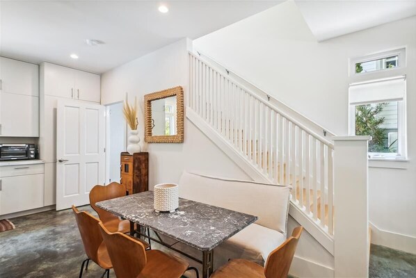 A modern kitchen with white cabinets, a dining table with chairs, and a staircase with white railings.