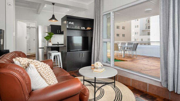 Ein modernes Wohnzimmer mit einer braunen Ledersofa, einem runden Couchtisch und Blick auf einen Balkon mit Gartenmöbeln.