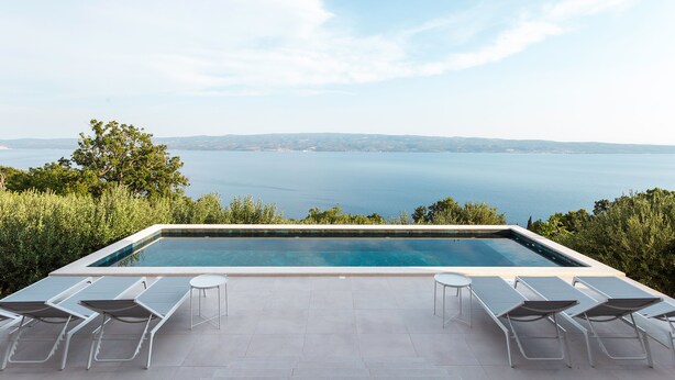 Una piscina a sfioro con lettini bianchi e vista sul mare.