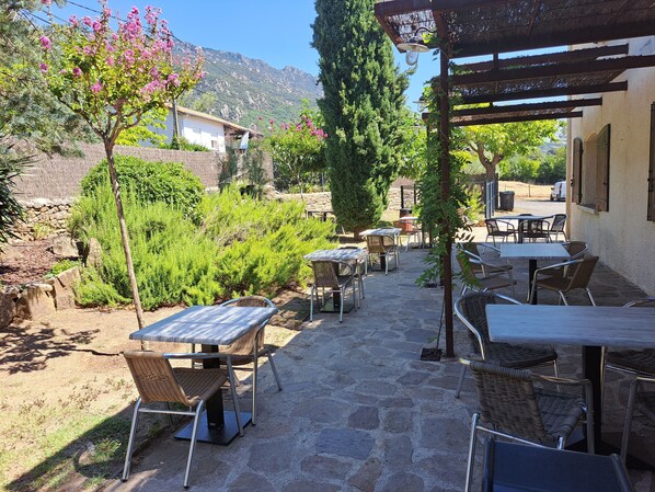 An outdoor patio area with stone flooring, wicker furniture, and a pergola. - L'Interlude (Mons)