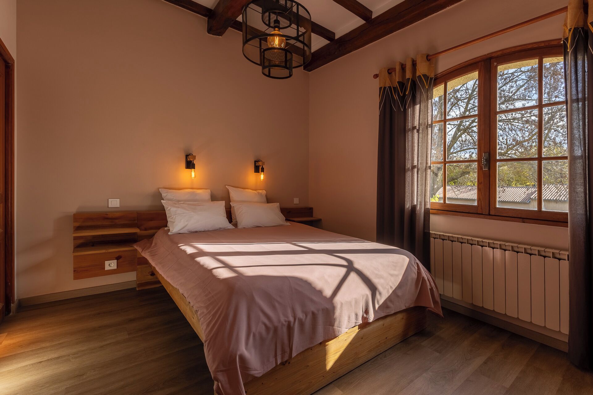 Un dormitorio con una cama de madera, dos lámparas de noche, una ventana con cortinas y un radiador.