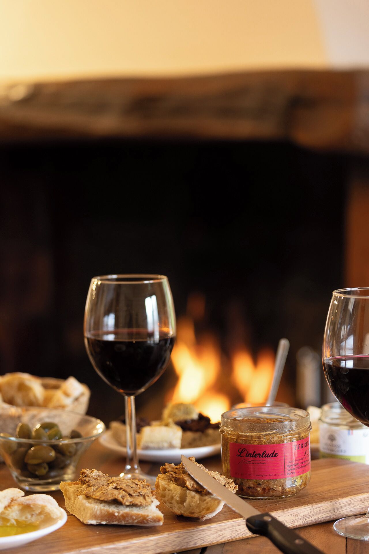 A table with a glass of red wine, a jar of spread, and bread.