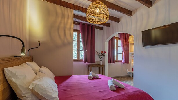 A bedroom with a large bed, wooden headboard, a bedside lamp, a TV, and a window with curtains.