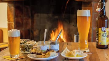 Una mesa con una botella de cerveza, dos vasos de cerveza, un cuenco de aceitunas y platos de comida.