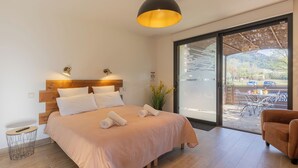 A bedroom with a large bed, a wooden headboard, a hanging light fixture, and a view of the outdoors through a sliding glass door.