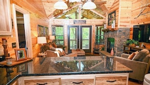 A log cabin interior with a central island, wooden cabinets, a fireplace, and a dining area.