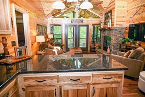 A log cabin interior with a central island, wooden cabinets, a fireplace, and a dining area.